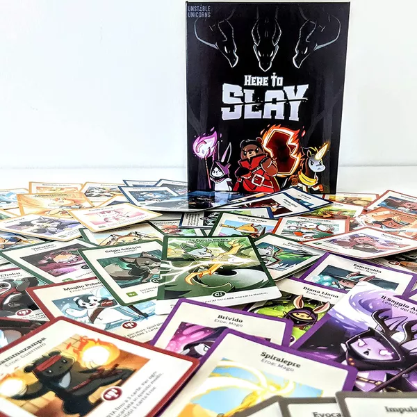 Here to Slay box, with several woodland creatures wielding glowing weapons. The box is surrounded by playing cards with a variety of other cute woodland creatures on them.